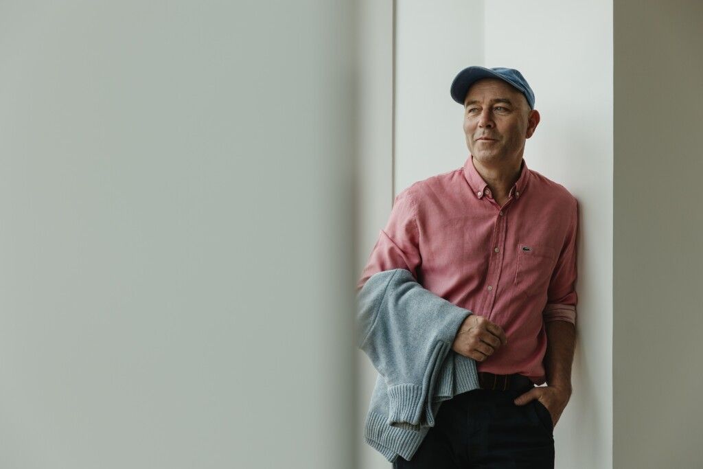 Alain Champenois wearing a pink shirt and blue baseball cap and looking into the distance.